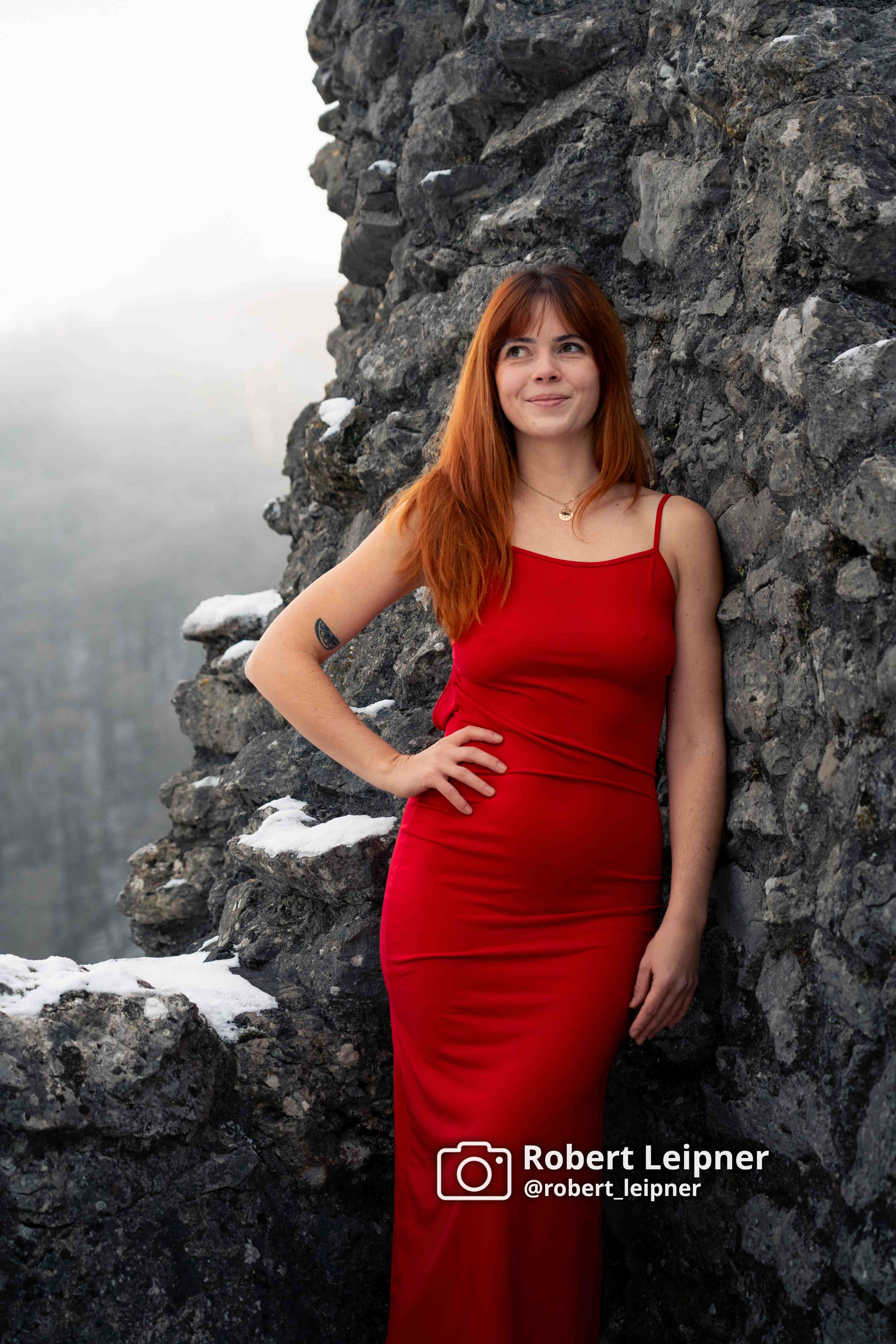 Model in rotem Kleid auf einer Burgruine im Winter
