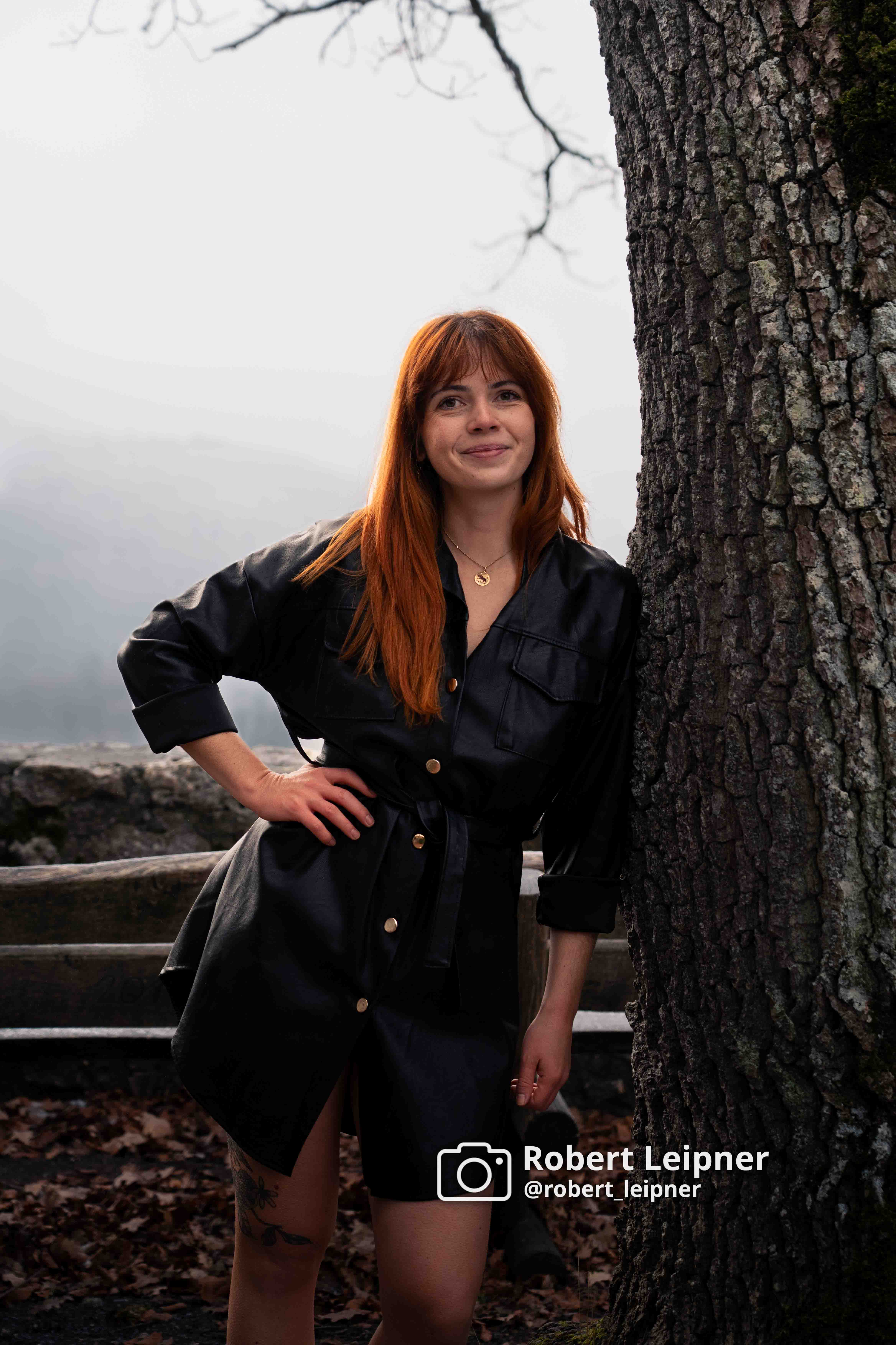 Model in schwarzer Jacke am Baum lehnend